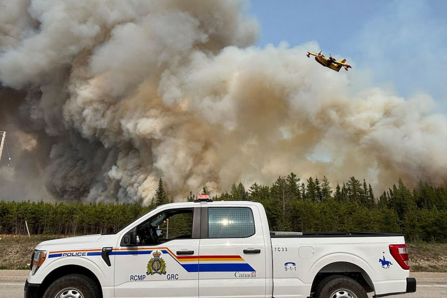 A Royal Canadian Mounted Police (RCMP) patrol vehicle is parked as a water bomber flies over the plume of smoke from a wildfire near The Pas, Manitoba, Canada May 27, 2025.