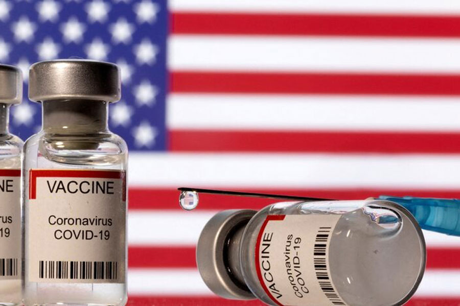 Illustration shows vials labelled "VACCINE Coronavirus COVID-19" and a syringe in front of a displayed US flag Vials labelled "VACCINE Coronavirus COVID-19" and a syringe are seen in front of a displayed US flag in this illustration taken December 11, 2021.
