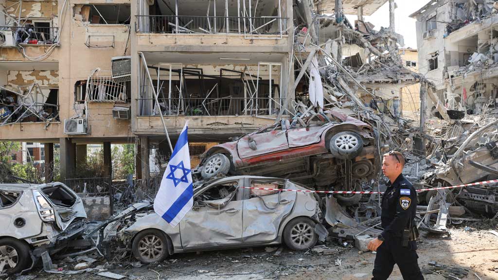 An Israeli police officer walks past damaged vehicles at an impact site following a missile attack from Iran on Israel, in Ramat Gan, Israel, June 14, 2025. REUTERS