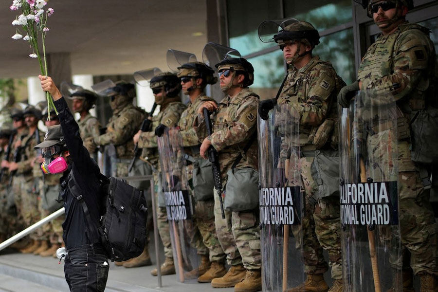 A demonstrator raises his hand holding flowers as members of the National Guard stand in formation outside a federal building during the No Kings protest against US President Donald Trump's policies, in Los Angeles, California, US, June 14, 2025.