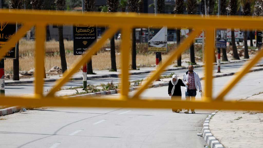 Palestinians walk behind a closed gate at the entrance of Turmus Ayya village near Ramallah, in the Israeli-occupied West Bank May 21, 2025. REUTERS/Mohamad Torokman
