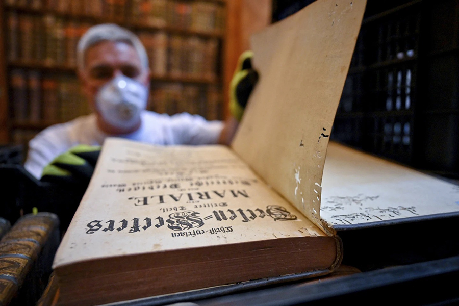 In this photo provided by Pannonhalma Archabbey, a restorer shows an old book with holes in its pages due to a drugstore beetle infestation, at the Pannonhalma Archabbey's library in Pannonhalma, Hungary on Thursday, July 3, 2025, as a beetle infestation threatens its ancient collection — Pannonhalma Archabbey via AP