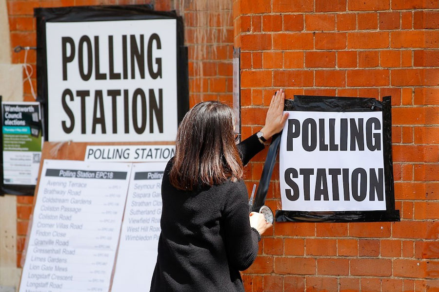A woman attaches a sign on the wall of a polling station, during the local elections in London, Britain May 5, 2022.