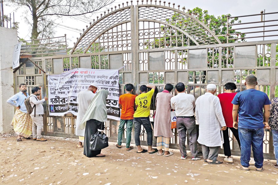 Curious onlookers try to peer through the main gate of Milestone School and College, where a Bangladesh Air Force jet crashed on Monday, killing a number of schoolchildren. The photo was taken on Wednesday