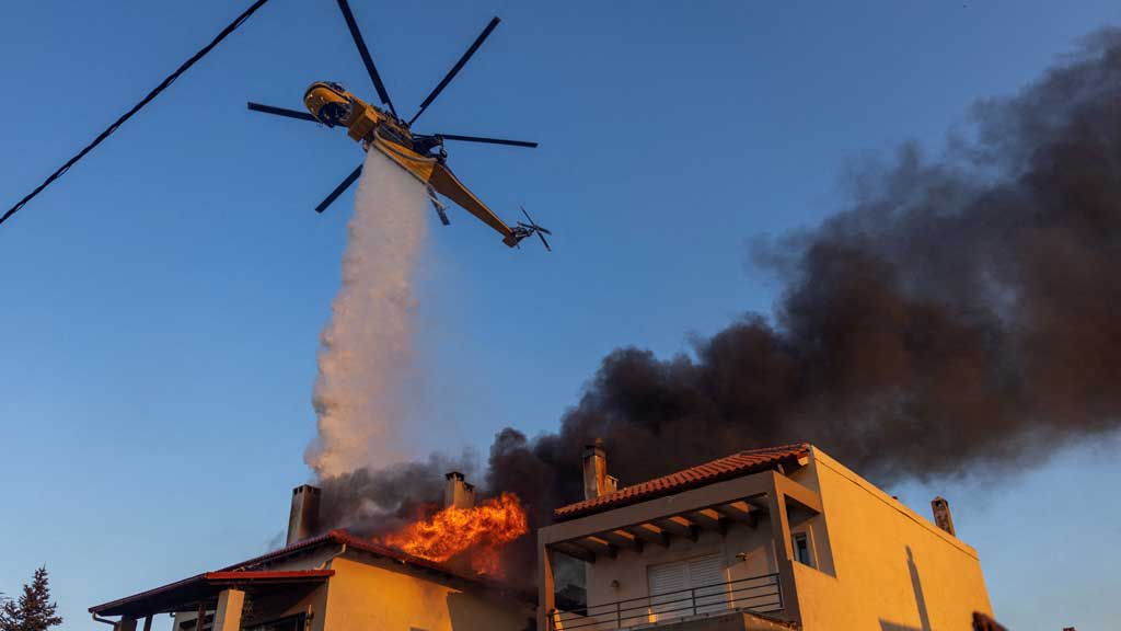 A firefighting helicopter makes a water drop on a burning house as a wildfire burns in the village of Kryoneri, near Athens, Greece, July 26, 2025. REUTERS