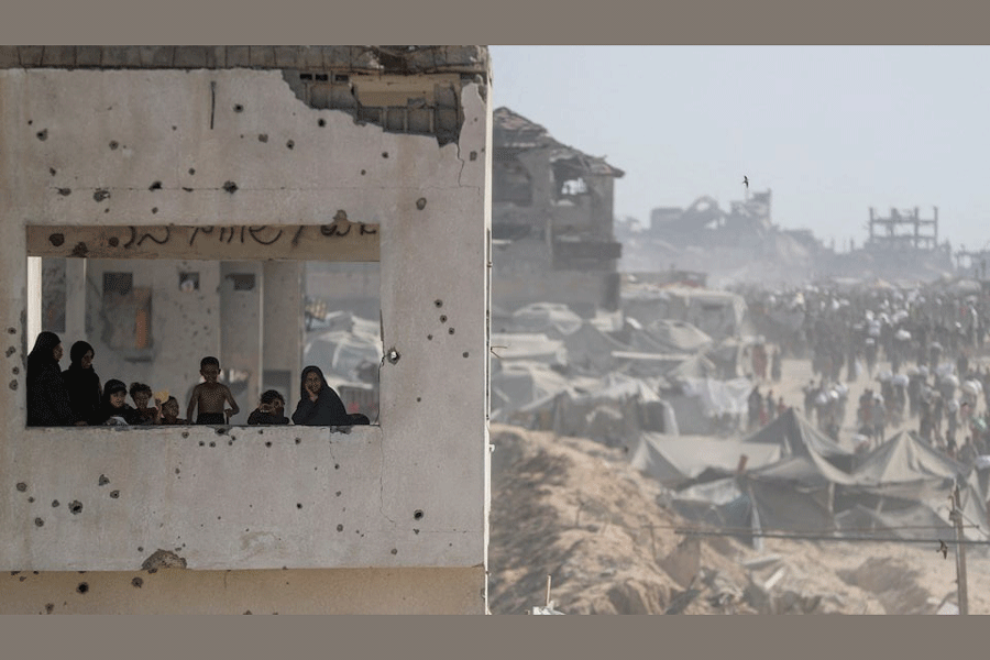 Women and children look out from a damaged building as Palestinians carry aid supplies that entered Gaza through Israel, in Beit Lahia, northern Gaza Strip, August 2, 2025.