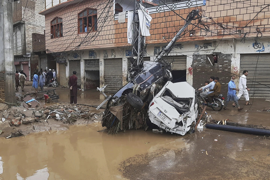 Residents walk next to damaged cars stuck to an electric pole following flash flooding due to heavy rains in a neighborhood of Mingora, the main town of Swat Valley, northwestern Pakistan, Friday, August 15, 2025 — AP photo