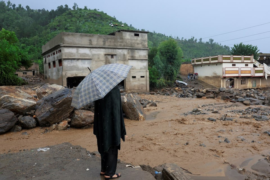 A resident stands with an umbrela as rain water flowing from mountains crosses a damaged area, following a storm that caused heavy rains and flooding in Bayshonai Kalay, in Buner district, in Khyber Pakhtunkhwa province, Pakistan, August 18, 2025.