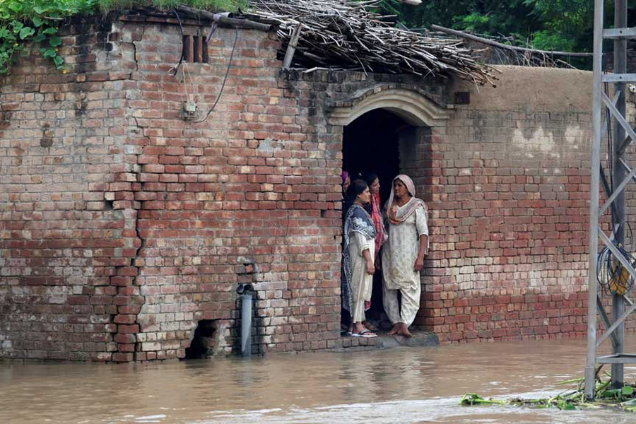 Residents stand at the entrance of a house on a flooded road, due to the monsoon rains and rising water level of the Sutlej River, in Hakuwala village near the Pakistan-India border in Kasur district of the Punjab province, Pakistan, Aug 24, 2025.