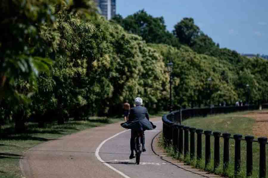 A man wearing a suit rides a bike through Hyde Park on a hot summer day, in London, Britain, Jun 16, 2025.