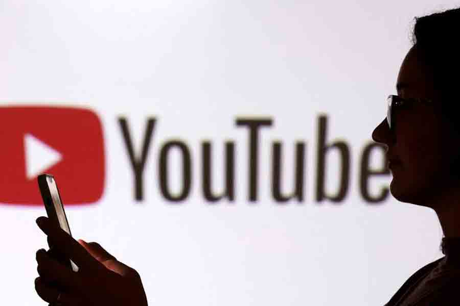 A teenager poses for a photo while holding a smartphone in front of a Youtube logo in this illustration taken Sept 11, 2025.