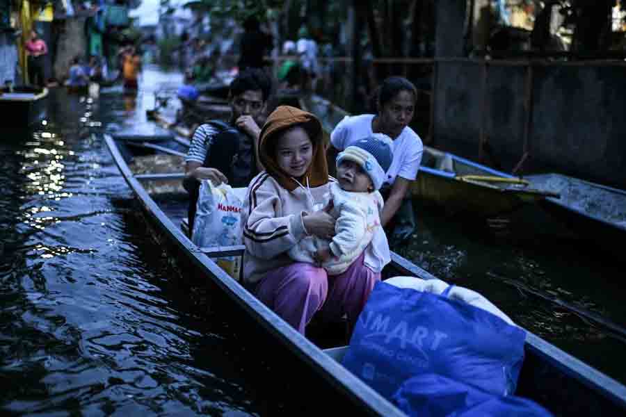 People ride on a boat to cross a flooded street following rains, intensified by Severe Tropical Storm Bualoi, in Dela Paz, Binan, Laguna province, Philippines, September 26, 2025.