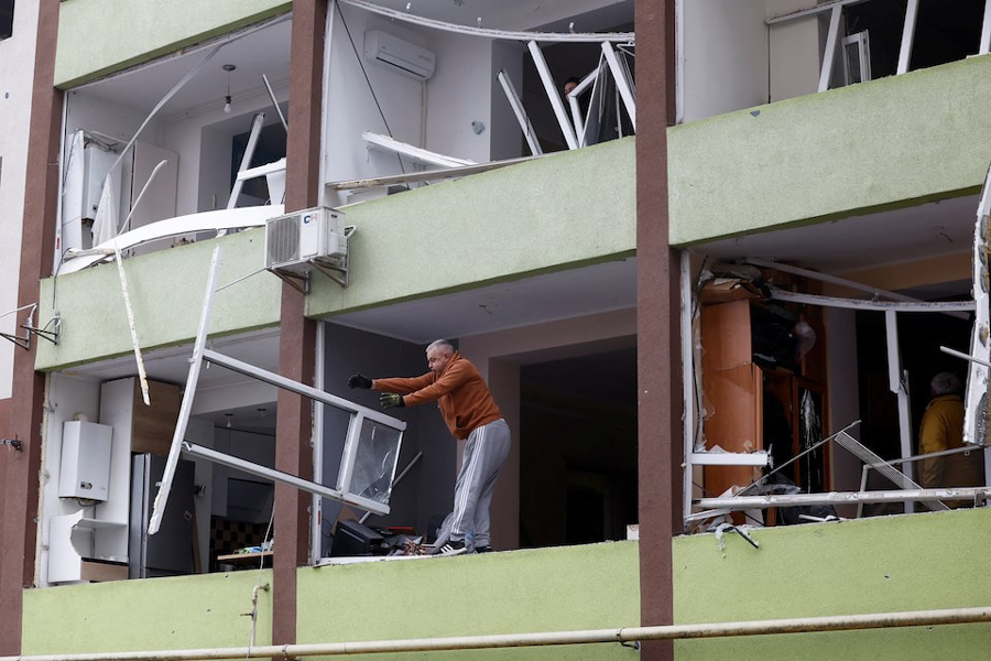 A man removes debris from a damaged building opposite to an impact site at a residential neighbourhood after overnight Russian drone and missile attacks in Kyiv, Ukraine, September 28, 2025.