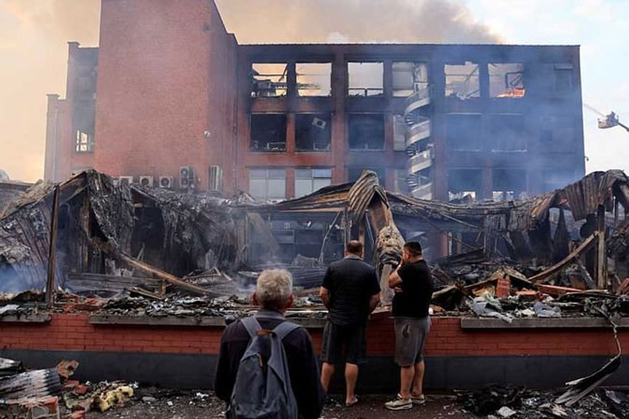 People look at a building of the Tessi group, burnt during night clashes between protesters and police, following the death of Nahel, a 17-year-old teenager killed by a French police officer in Nanterre during a traffic stop, at the Alma district in Roubaix, northern France, June 30, 2023.