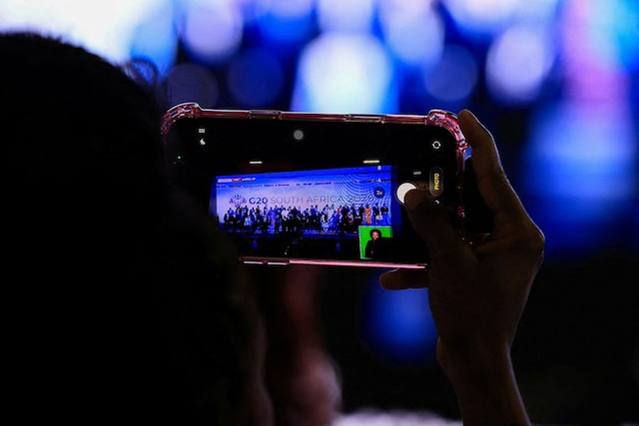 A person uses their phone to capture the leaders family photo on a big screen, on the opening day of the G20 leaders' Summit at the Nasrec Expo Centre in Johannesburg, South Africa, November 22, 2025.