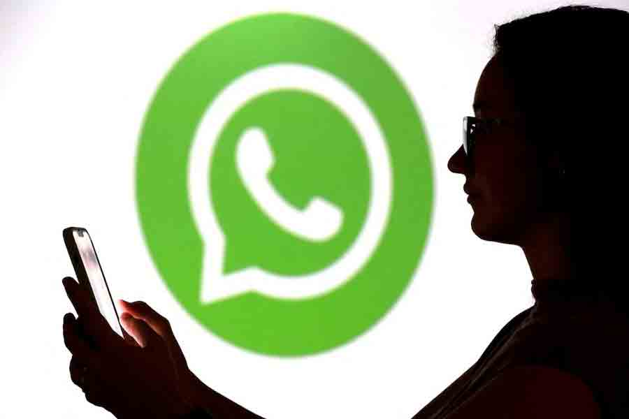 A teenager poses for a photo while holding a smartphone in front of a Whatsapp logo in this illustration taken September 11, 2025.