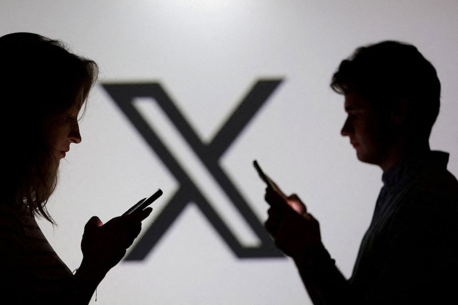 Teenagers pose for a photo while holding smartphones in front of a X logo in this illustration taken September 11, 2025.