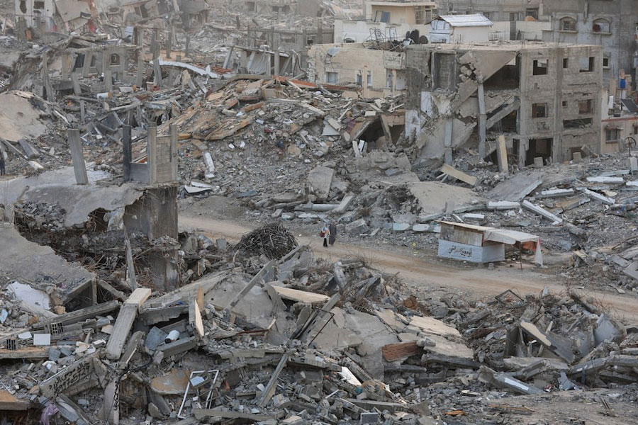Palestinian women walk among piles of rubble and damaged buildings, in Gaza City, November 24, 2025.