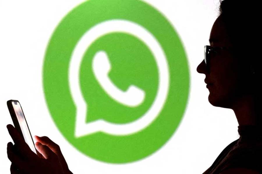 A teenager poses for a photo while holding a smartphone in front of a Whatsapp logo in this illustration taken Sept 11, 2025.