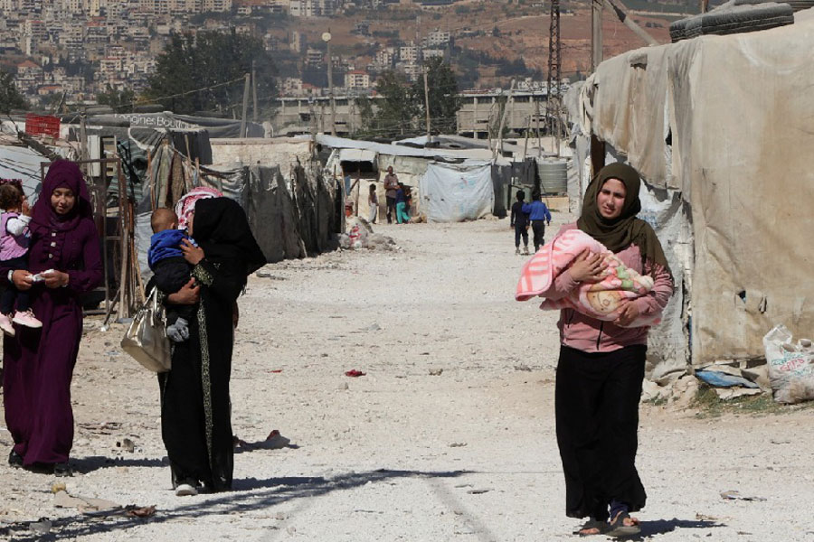 Syrian refugee women carry children as they walk at an informal camp, in the Bekaa Valley, Lebanon Oct 18, 2022.