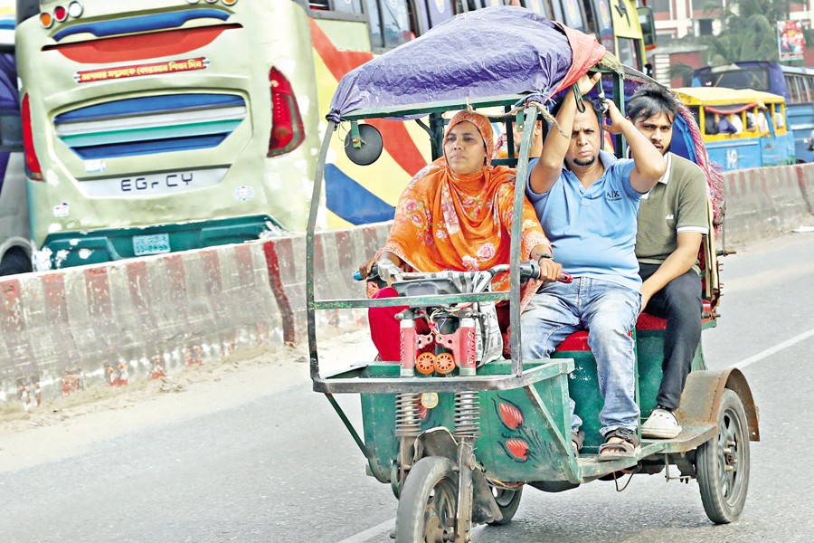 A woman drives a battery-run autorickshaw carrying passengers across Babubazar Bridge in the capital. Alongside men, a growing number of women in Dhaka are taking up such work to earn a livelihood. The photo was taken recently ahead of International Women's Day — FE photo by Shafiqul Alam