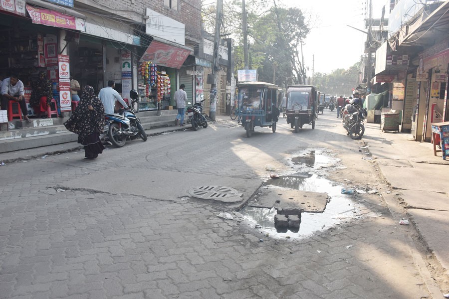 The photo shows sinking uni-block road and raised manhole covers creating potholes and waterlogging near District Judge Court-Model High School stretch in Manikganj district - FE Photo