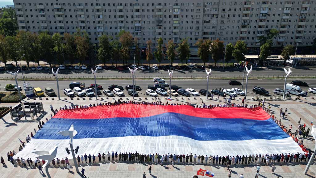A drone view shows people holding a large-size Russian state flag during celebrations of National Flag Day in Mariupol, a Russian-controlled city of Ukraine, Aug 22, 2025.
