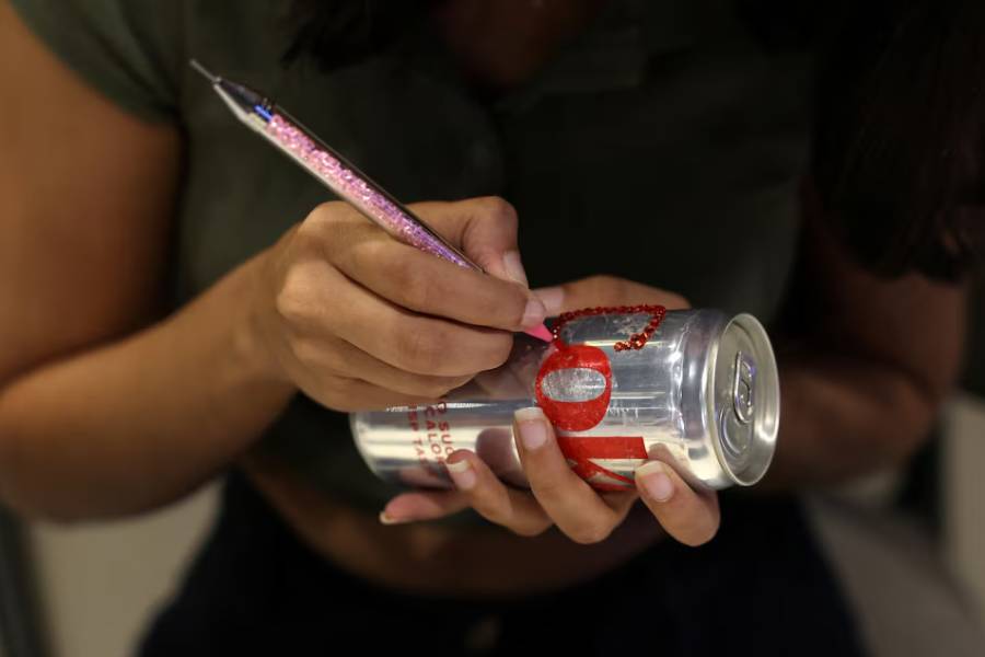 A woman uses rhinestones to decorate a diet coke can for an upcoming Diet Coke party to attract fans of the beverage amid an aluminium can shortage caused by disruption from the U.S. and Israel's war with Iran, inside Art Cafe at Broadway store in New Delhi, India, May 5, 2026.