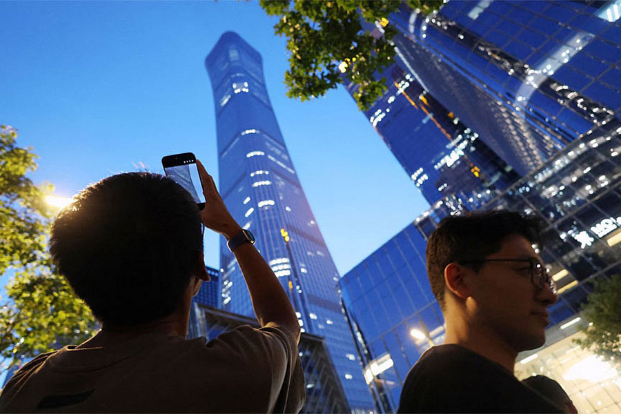 A man points a mobile phone at CITIC Tower, also known as China Zun, where damage is visible on a high floor of the exterior, in Beijing, China Jun 26, 2026.