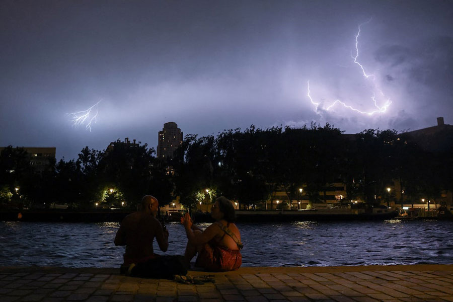 People sit on the banks of the Bassin de la Villette during a storm, as lightning strikes behind them amid a heatwave in Paris, France, June 27, 2026.