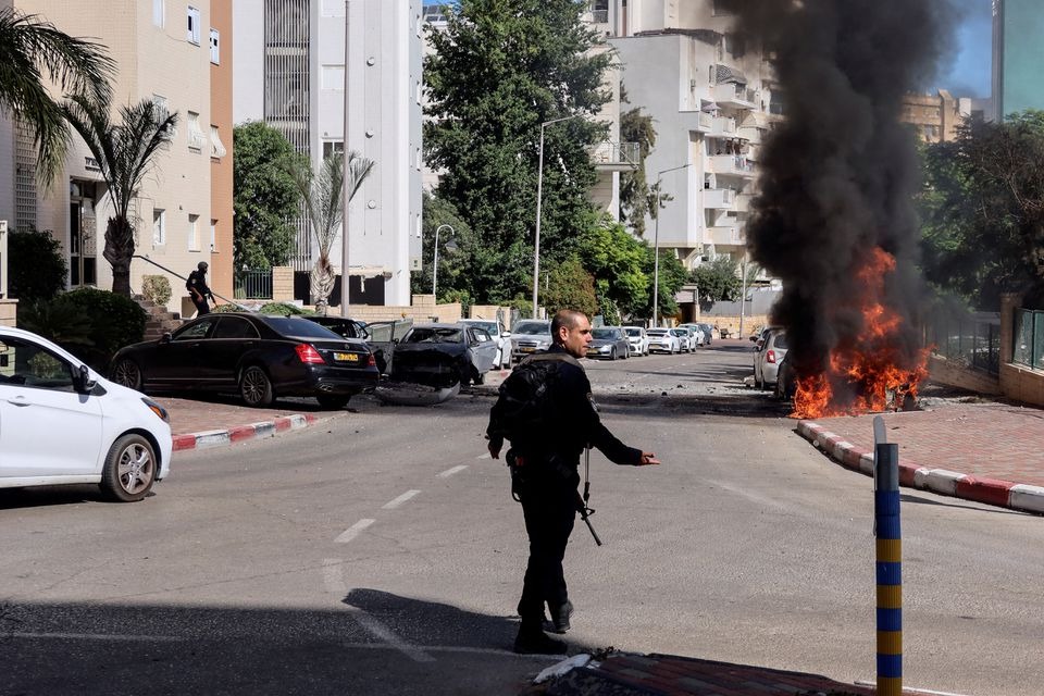 A member of Israel's police forces walks towards a fire as rockets are launched from the Gaza Strip, in Ashkelon, southern Israel on October 7, 2023 — Reuters photo