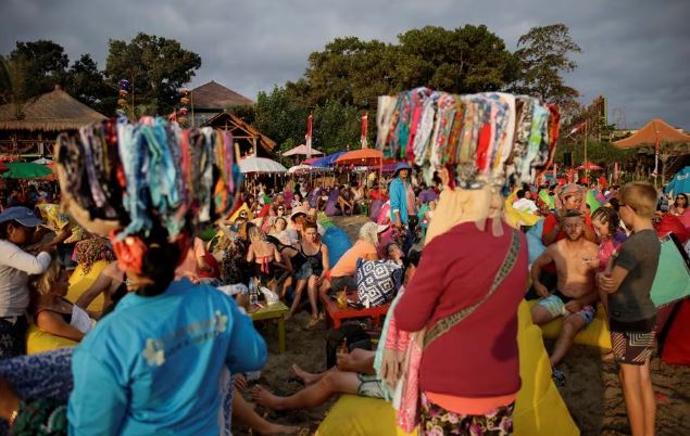 Vendors sell bandanas as tourists watch the sunset on Seminyak beach in Bali, Indonesia August 17, 2017. REUTERS/Thomas White/File Photo