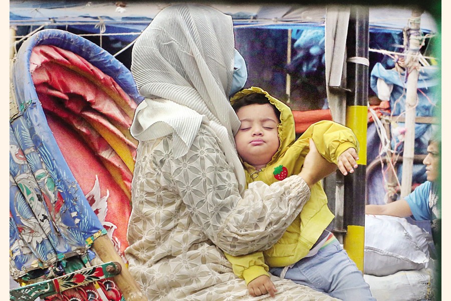 Wrapped in warm layers, a child sleeps soundly in his mother's lap as they travel by rickshaw in Dhaka's crowded Gulistan area on Tuesday. — FE photo by KAZ Sumon