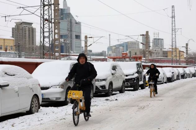 People ride bicycles on a road covered by snow following snowfall in Beijing, China December 15, 2023. REUTERS/Tingshu Wang/File Photo