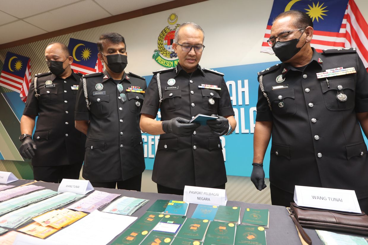 Johor Immigration director Baharuddin Tahir (second from right) going through a passport, which is some of the seized items made on Ops Serkap during a press conference held at state Immigration headquarters in Home Ministry Complex in Setia Tropika, Johor Baru here on Wednesday (Dec 20). — THOMAS YONG/The Star