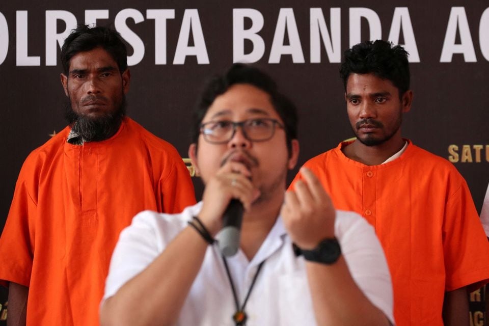 Two suspects, a Bangladesh national and a Rohingya, stand while an Aceh police official, Fadillah Aditiya Pratama speaks during a news conference, after smuggling at least 400 Rohingyas refugees in early December, at a police office in Banda Aceh, Aceh province, Indonesia on December 27, 2023 — Antara Foto via REUTERS