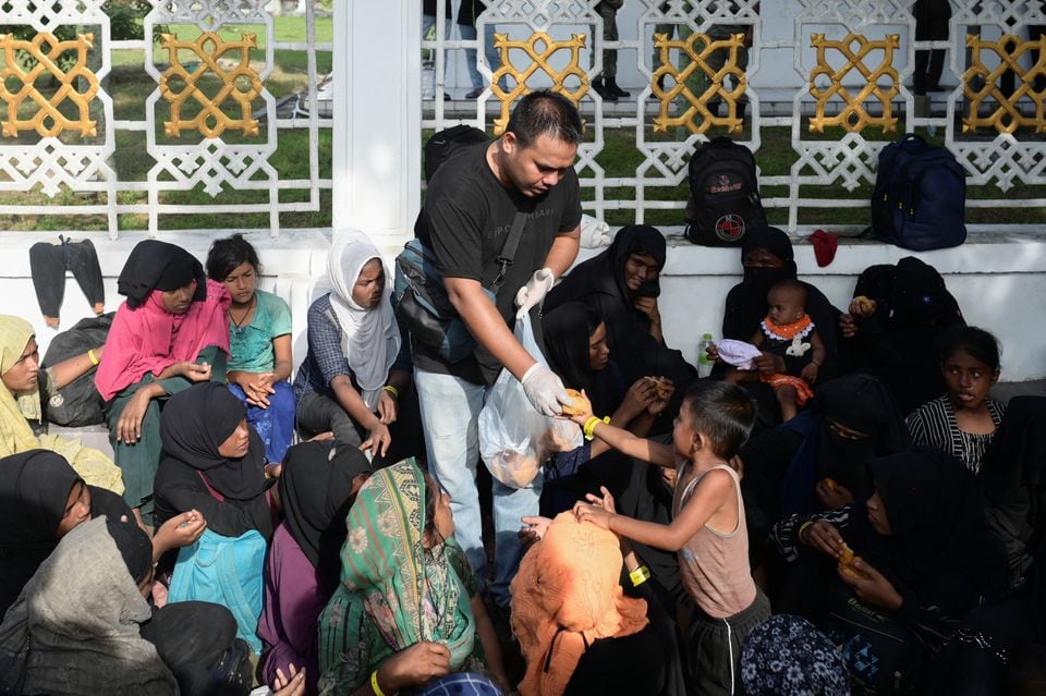 Rohingya Muslim refugees receive food as they take rest on a sidewalk outside the government office after they were refused shelter by local residents, following their arrival, in Banda Aceh, Indonesia, December 11, 2023. REUTERS/Riska Munawarah/File Photo