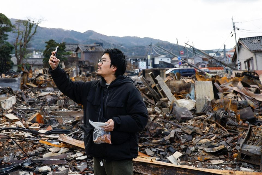 Japanese lacquer artist Kohei Kirimoto takes photos, while searching for his cats, next to an “Asaichi” morning market which burnt down in a quake-triggered fire, in Wajima, Japan, January 4, 2024.