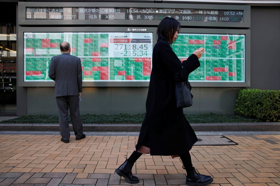 A woman walks past a man examining an electronic board showing Japan’s Nikkei average and stock quotations outside a brokerage, in Tokyo, Japan, March 20, 2023.