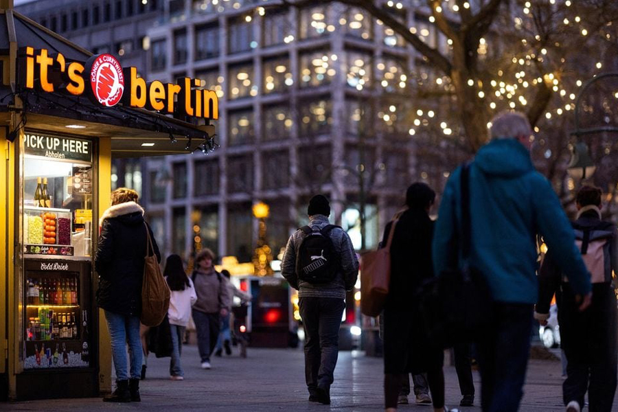 People walk next to a Doner kebab and Currywurst booth at Kurfuerstendamm shopping street during Christmas season in Berlin, Germany, December 18, 2023.