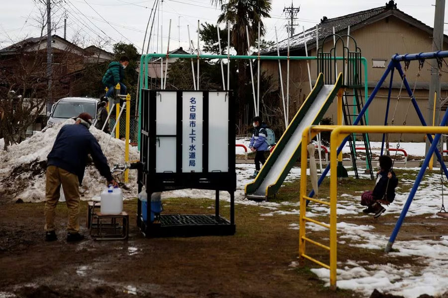 Children play in the playground as a local resident refills a bottle from the communal water tank for Noto earthquake survivors in Suzu, Ishikawa Prefecture, Japan, January 30, 2024.