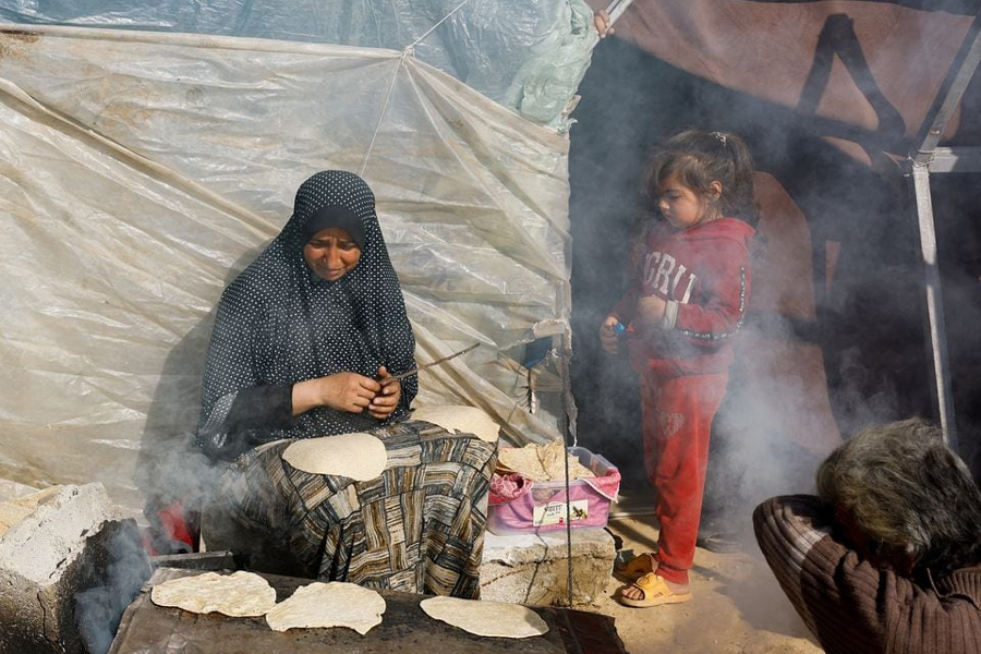 A child stands next to a cooking woman, as displaced Palestinians, who fled their houses due to Israeli strikes, shelter in a tent camp near the border with Egypt, amid the ongoing conflict between Israel and the Palestinian Islamist group Hamas, in Rafah in the southern Gaza Strip, December 11, 2023.