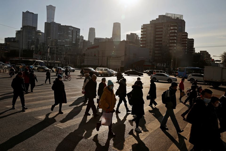 People cross a street during morning rush hour in front of the skyline of the central business district (CBD) in Beijing, China, December 15, 2020.