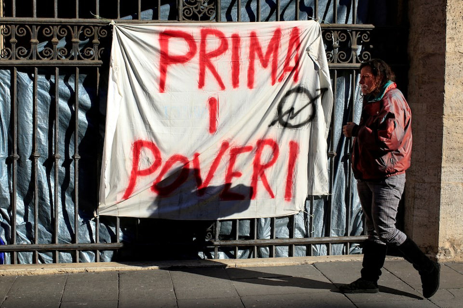 Angela Grossi walks past a banner reading “Poor first”, hanging in a gate of the portico of the Basilica of the Santi Apostoli, where she lives after being evicted from an unused building along with other families in August 2017, in Rome, Italy January 29, 2018.