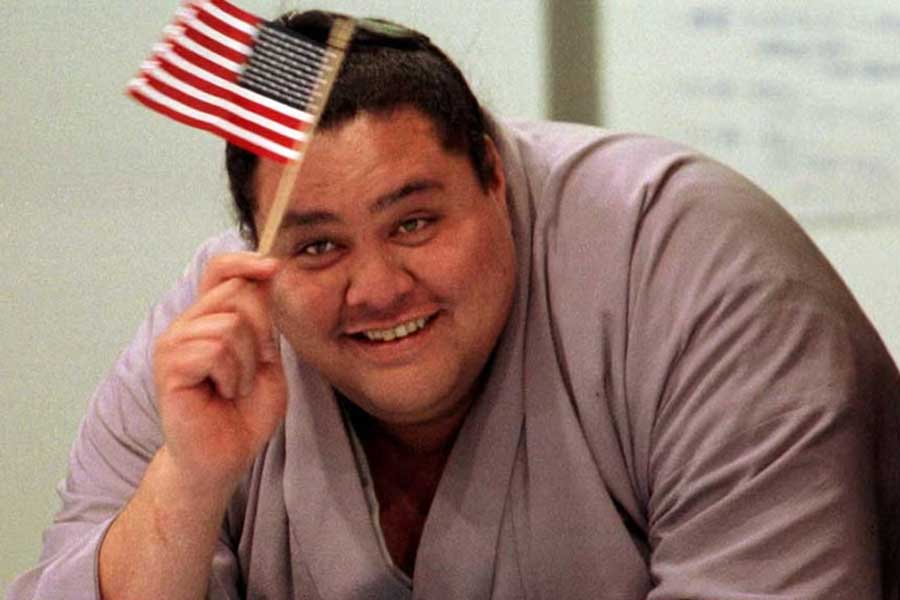 US born Grand Champion sumo wrestler Akebono waves an American flag as he watches US skaters at the White Ring Stadium in Nagano Feb 5,1998 ahead of the XVIII Winter Olympics.