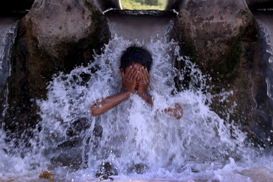 A boy cools off under a water pipe from a canal during a hot summer day on the outskirts of Peshawar, Pakistan, May 28, 2024.