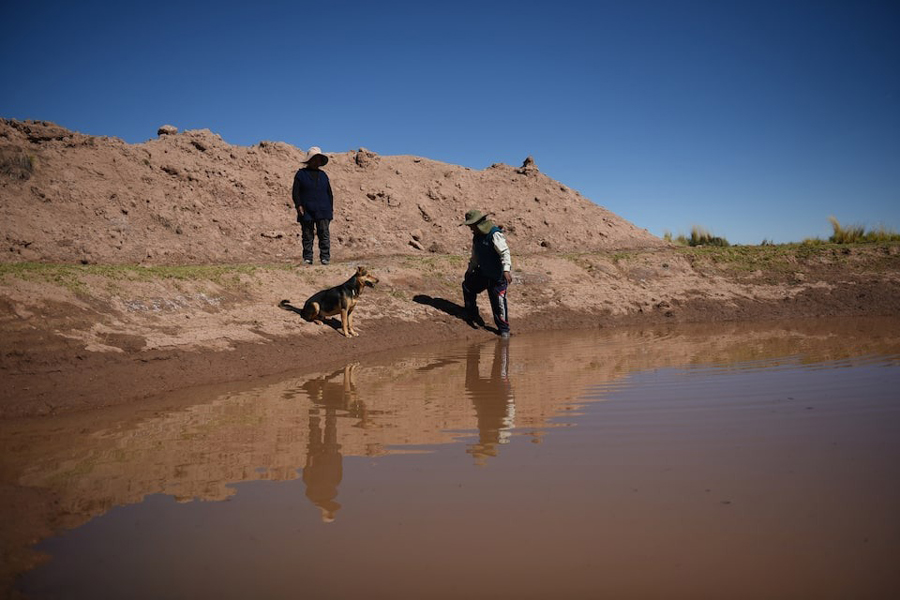 Edwin Churata and Elizabeth Churata walk past an artificial lagoon used for highland water storage, as Bolivian farmers modernize their techniques to meet climate challenges, in Sorachico, near Oruro, Bolivia, May 21, 2024.