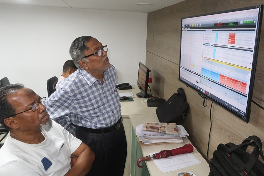 Investors react while monitoring stock price movements on TV and computer screens at a brokerage house in Dhaka city