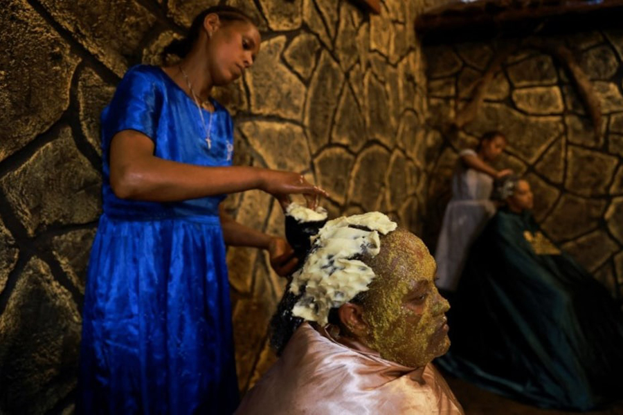 A traditional masseuse applies butter on the hair of her customer, at the Fana "Weyba Tis" beauty salon, in Addis Ababa, Ethiopia, May 14, 2024.