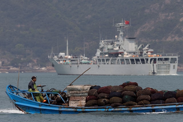 A fishing boat sails past a Chinese warship during a military drill off the Chinese coast near Fuzhou, Fujian Province, across from the Taiwan-controlled Matsu Islands, China, April 11, 2023. REUTERS/Thomas Peter/File Photo